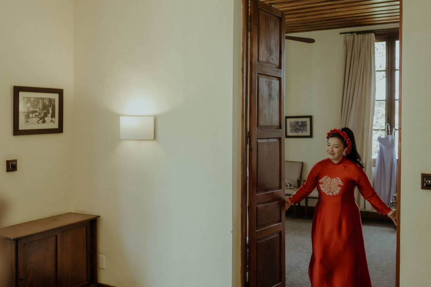 A bright red vintage style dress stands out against cream walls in a doorway between classic wooden-framed rooms.