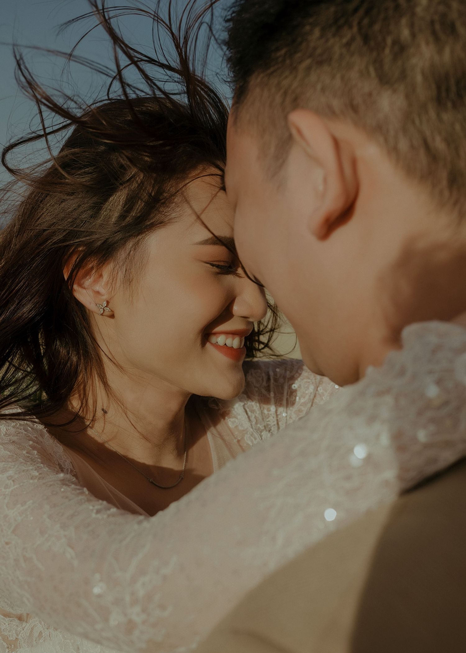 Intimate couple sharing a romantic moment during golden hour as wind blows through her hair.