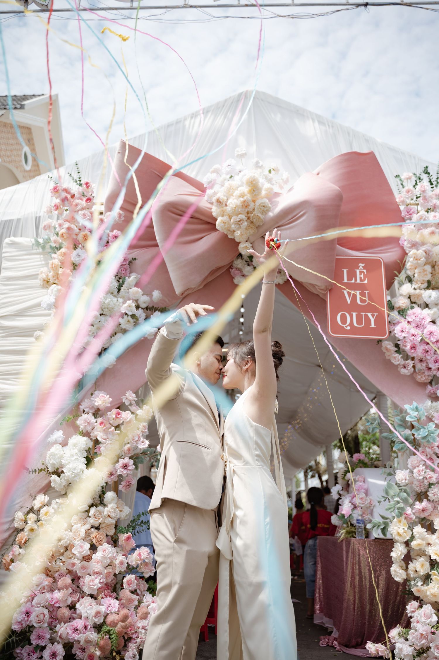 An elegant outdoor wedding ceremony with a pink bow archway decorated in cherry blossoms and white floral arrangements.