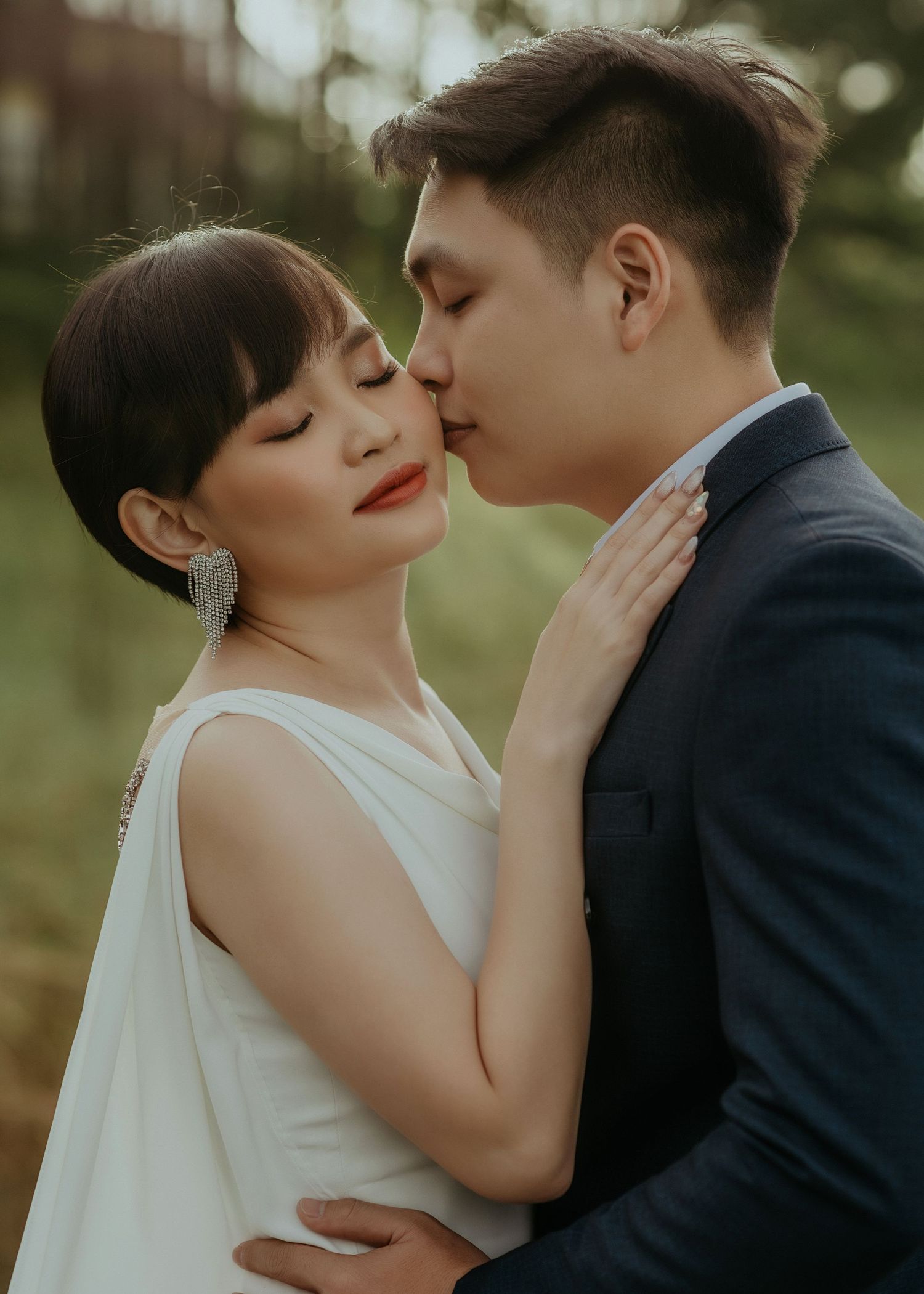 A romantic wedding photo shows a couple in white and navy sharing an intimate moment in a lush outdoor setting.
