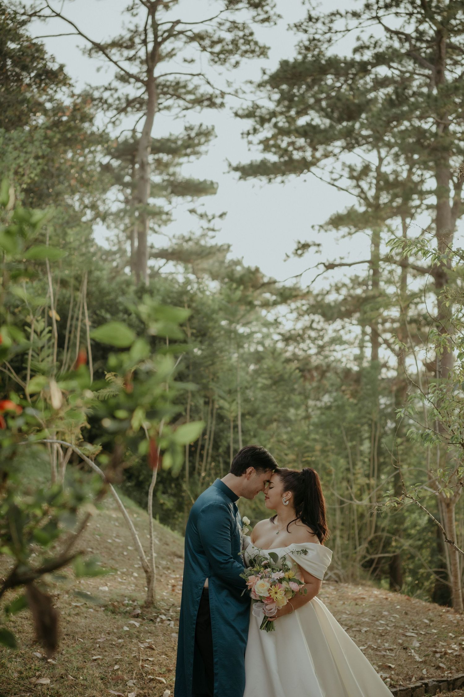 A romantic wedding couple embraces in a dreamy evergreen forest setting wearing elegant blue and white attire.