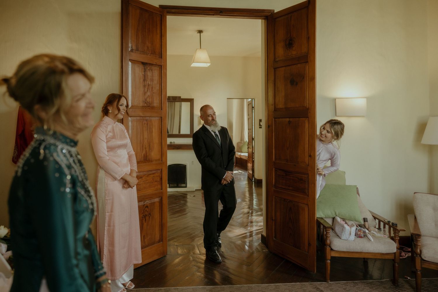 Guests gather in an elegant room with wooden double doors, soft lighting, and a warm interior during a formal event.