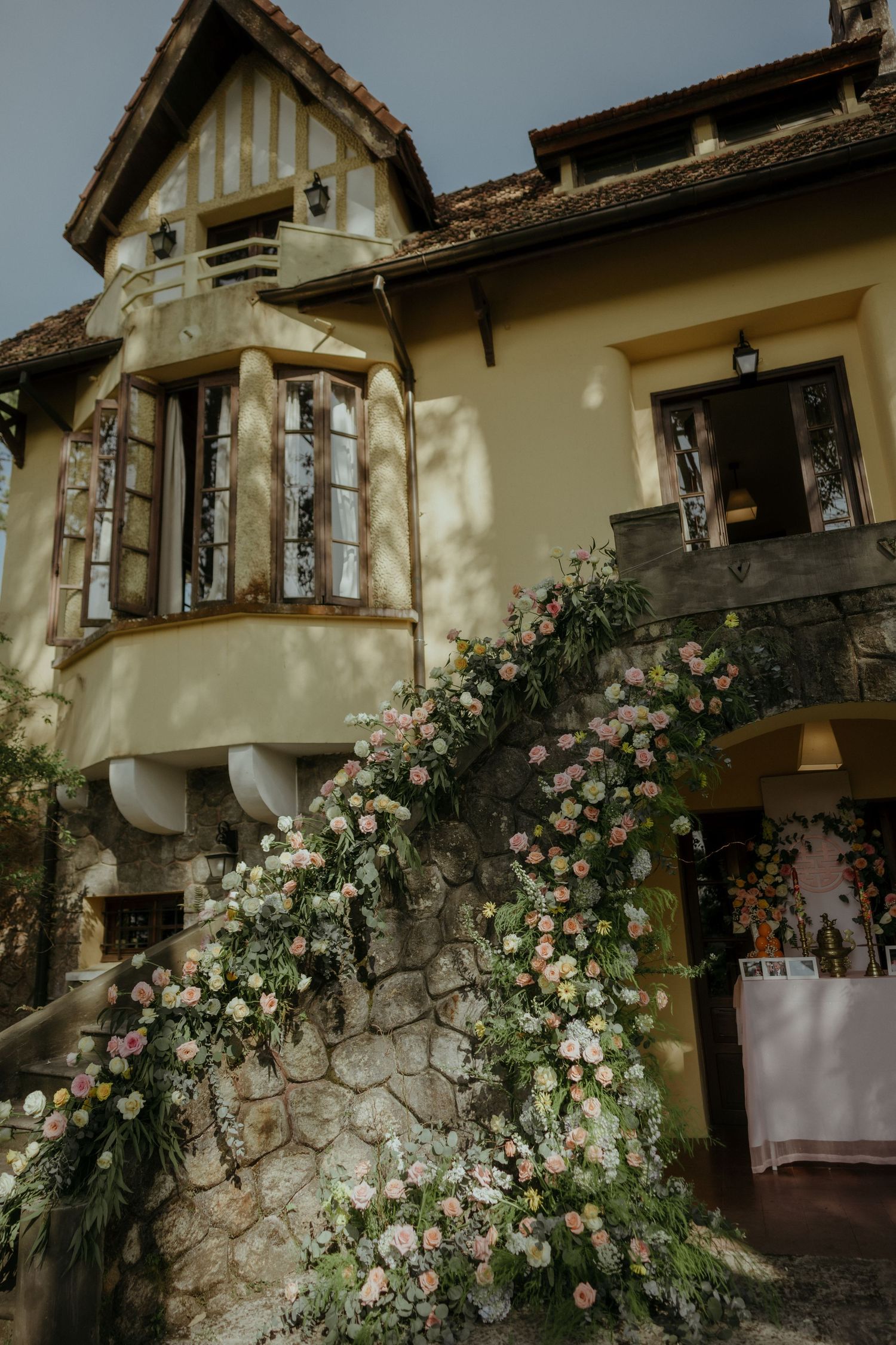 Rustic stone cottage with climbing roses features Tudor-style architecture and a charming curved stairway entrance.