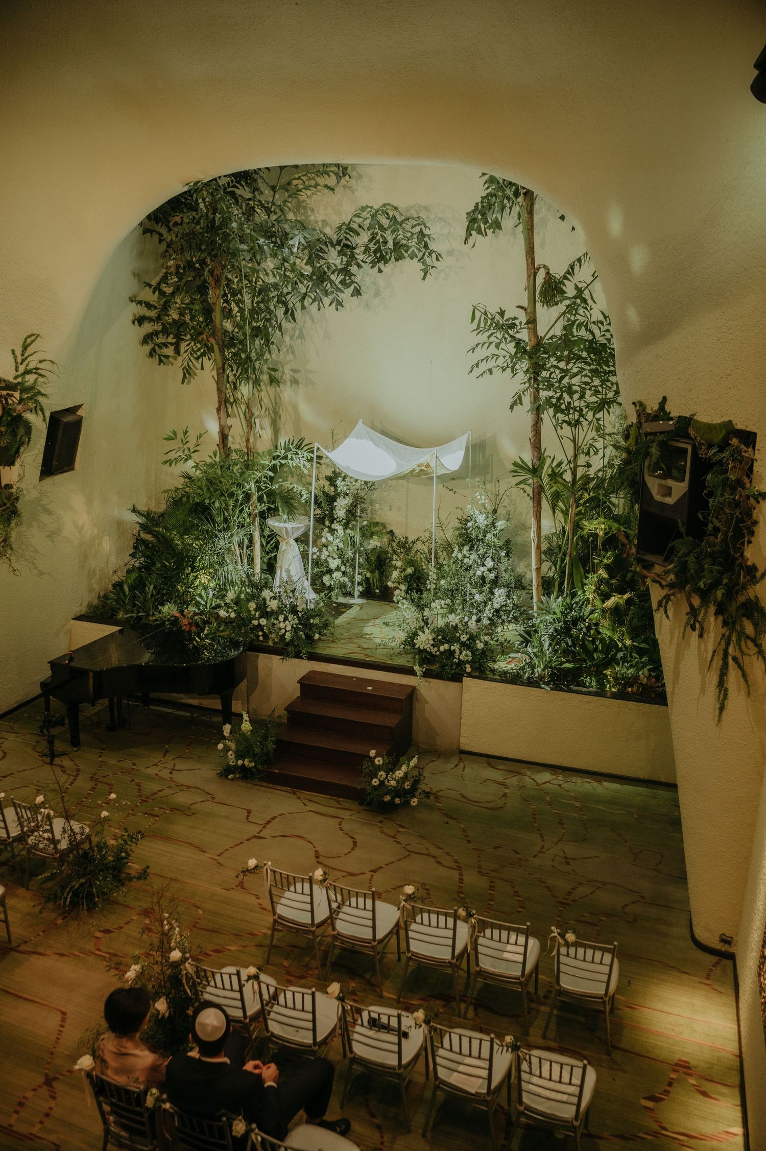 Indoor wedding venue decorated with hanging plants and white ceremony canopy.