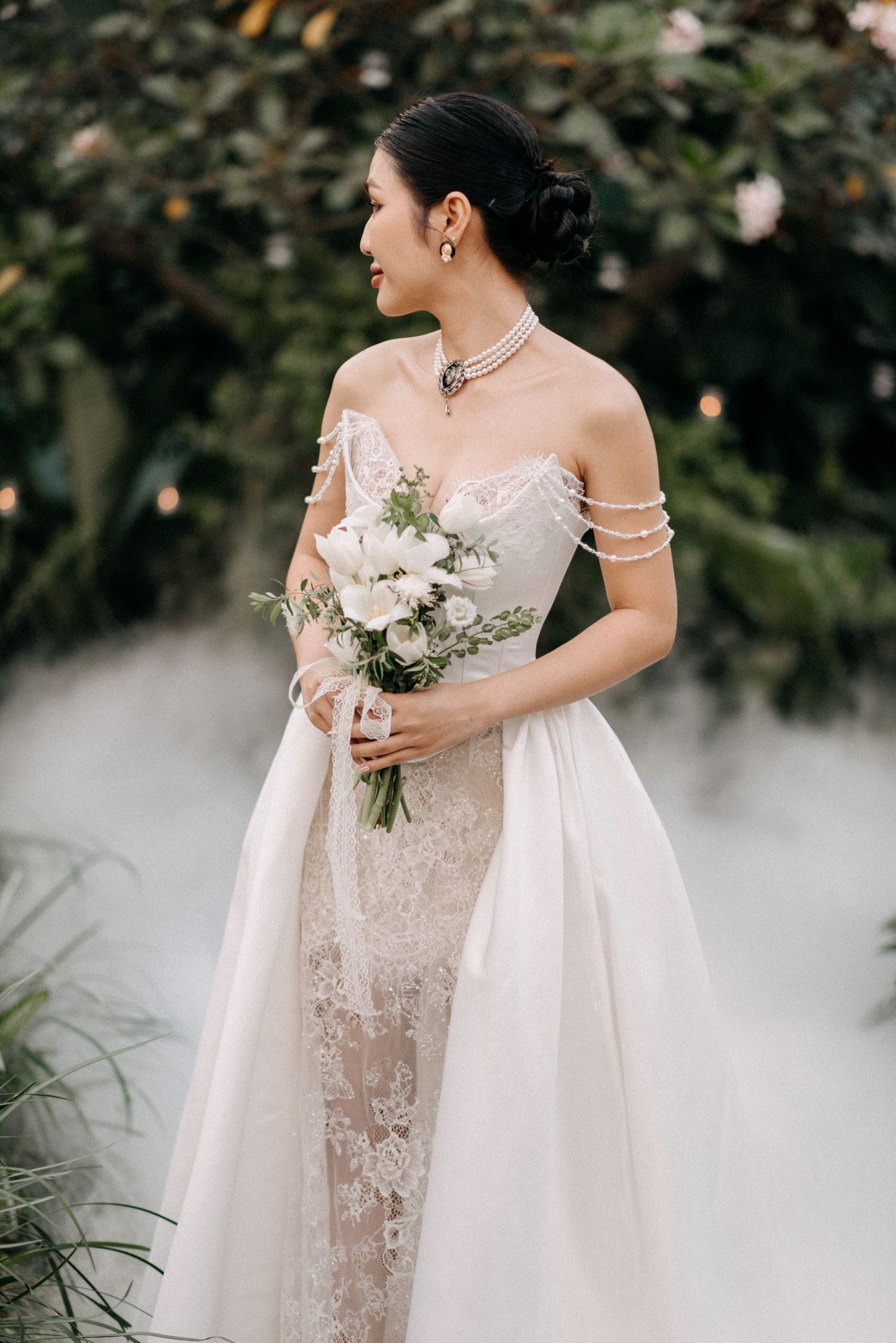 Side view of person wearing strapless lace wedding gown holding delicate white bouquet.