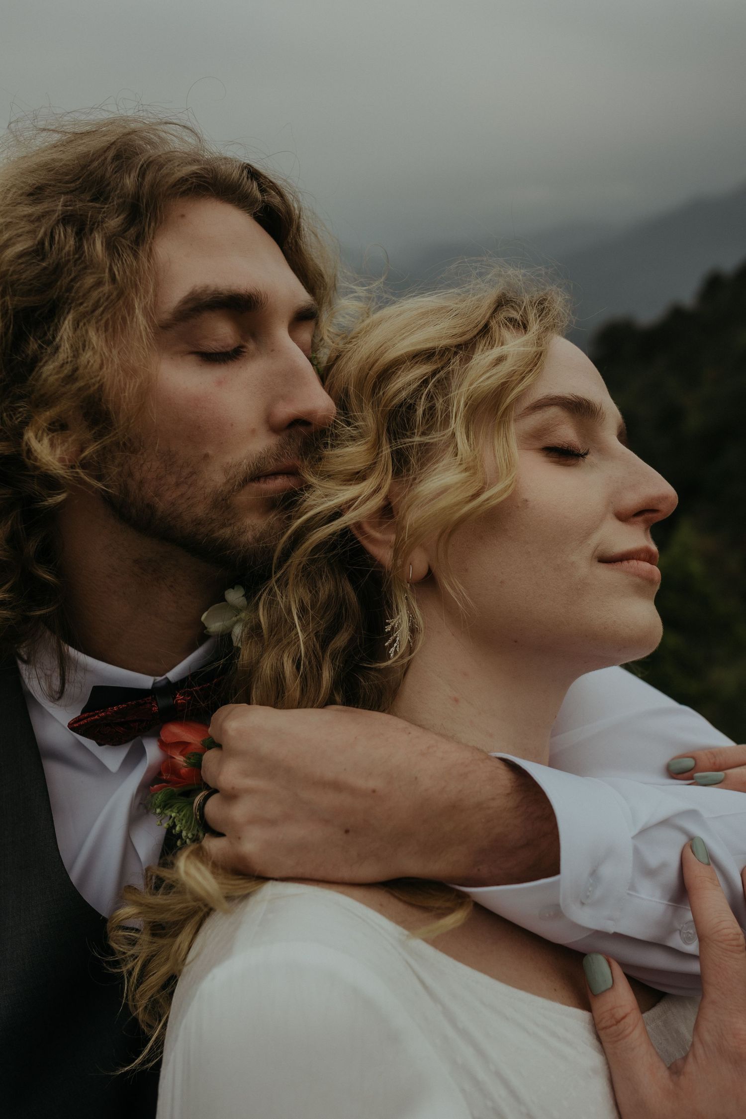 An intimate close-up portrait of a couple sharing a tender moment against mountain scenery.