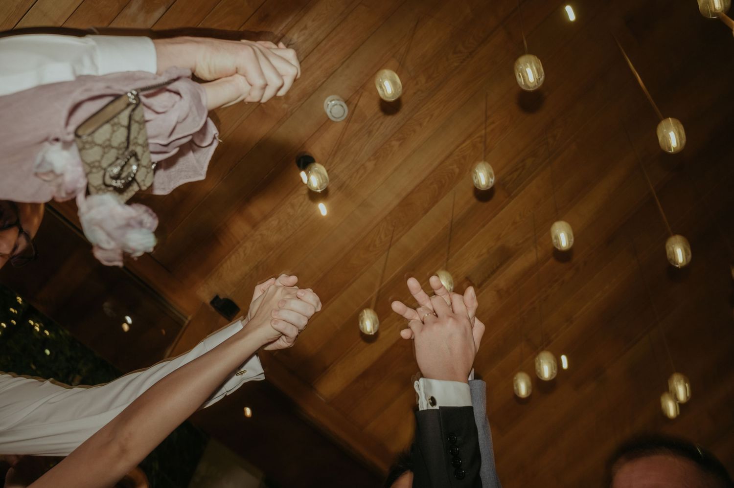 Hands raised in celebration with string lights creating a magical atmosphere on wooden ceiling.