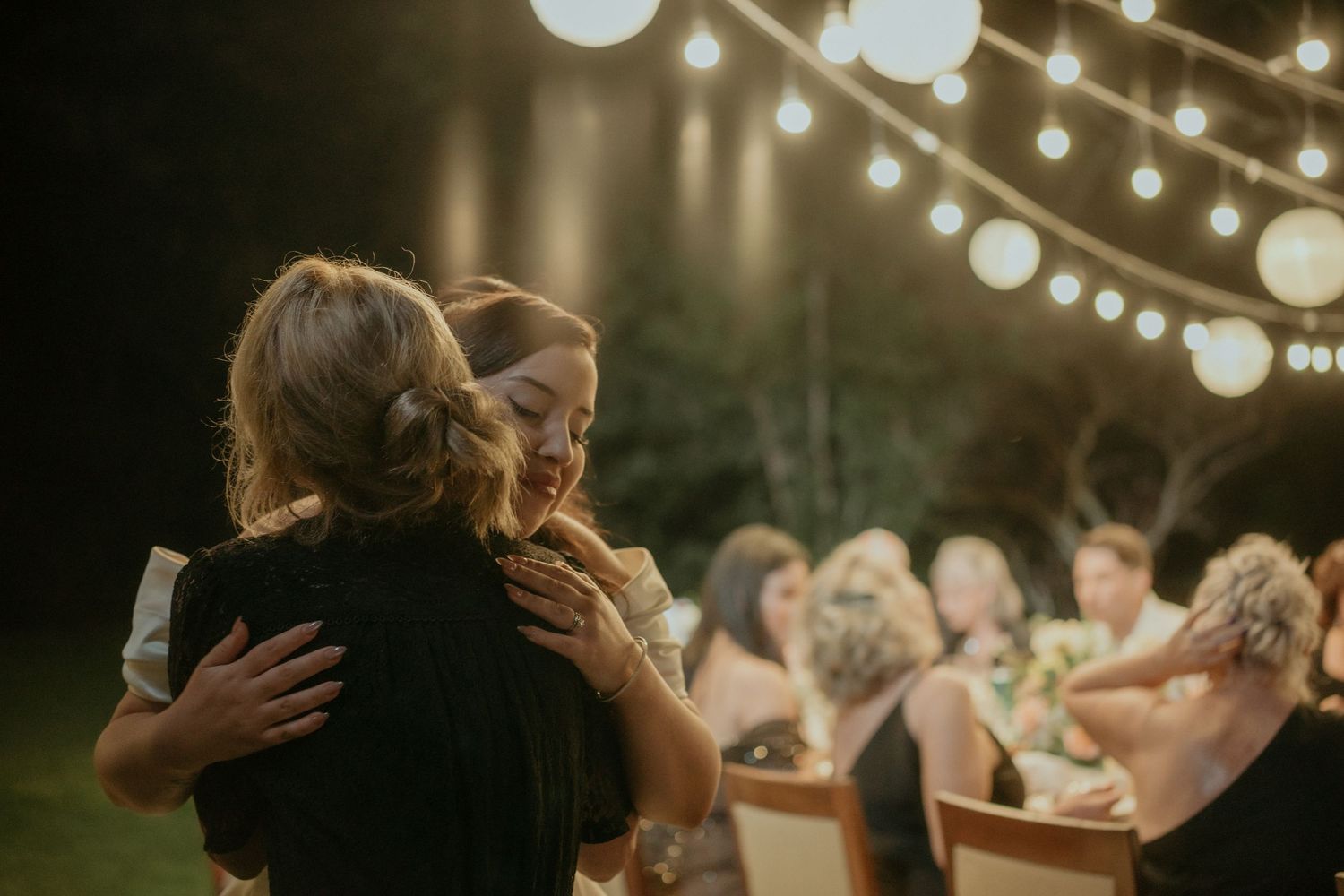 People dancing at an outdoor evening wedding reception with string lights illuminating the scene.