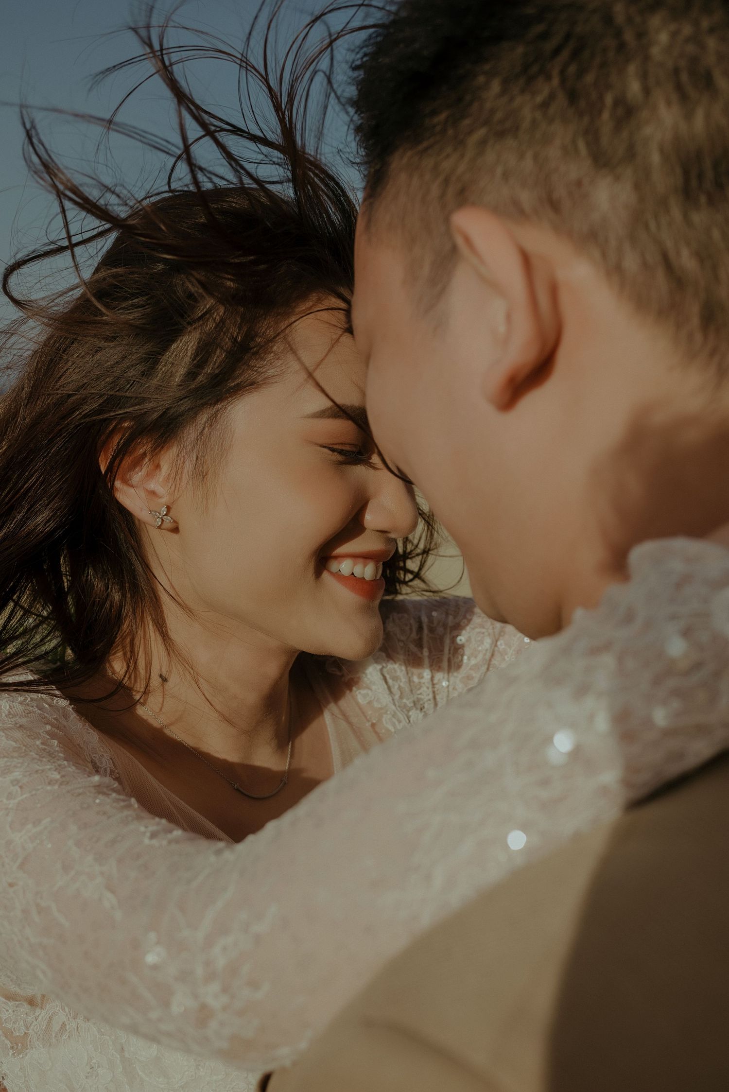 Intimate moment between couple embracing with wind-blown hair during golden sunset.