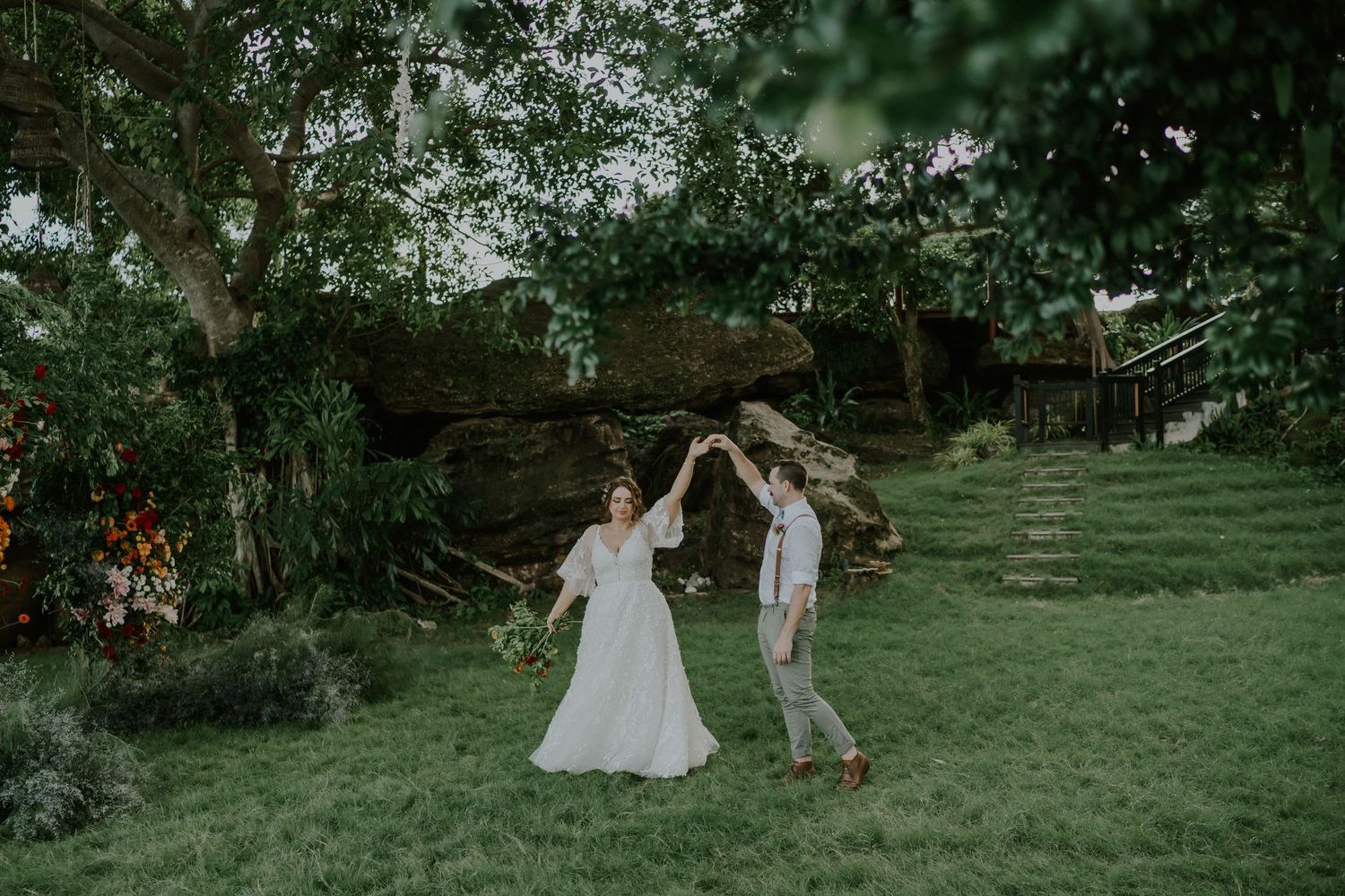 Couple dances playfully on green lawn during outdoor wedding celebration.