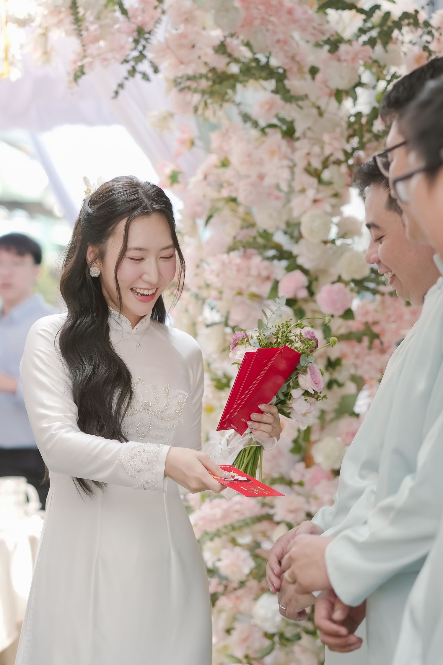 Traditional Vietnamese wedding ceremony with couple exchanging red envelopes under cherry blossoms.
