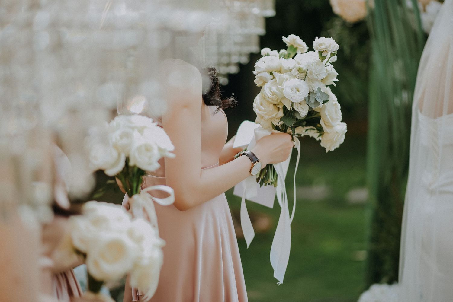 White floral bouquets with ribbon details held during an outdoor wedding ceremony.