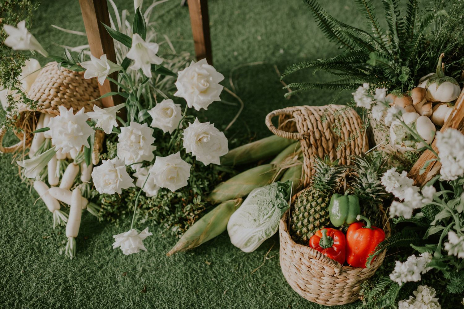White flowers and fresh produce arranged in woven baskets on artificial grass.
