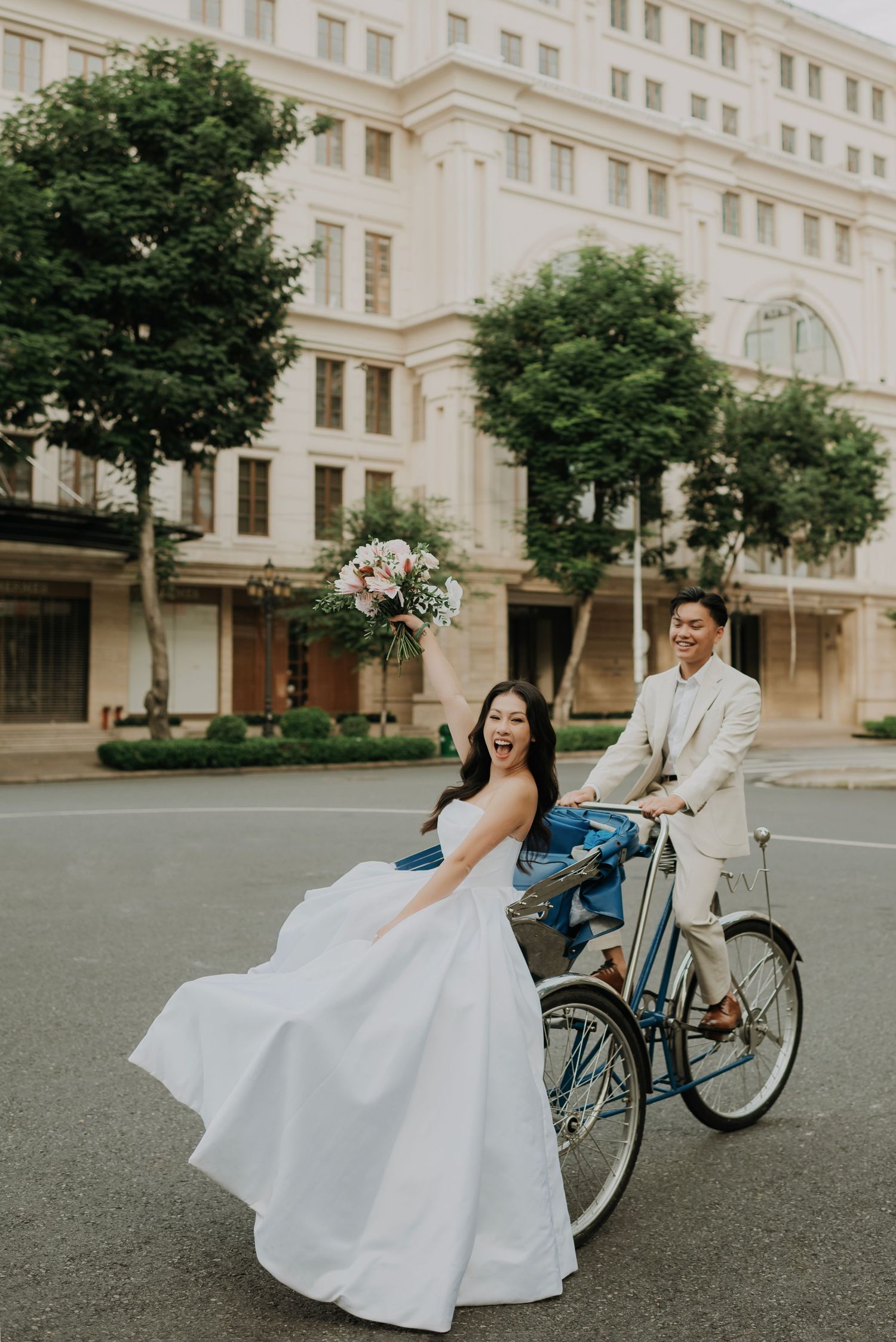A couple poses with a vintage bicycle for wedding photos in front of a classic building.