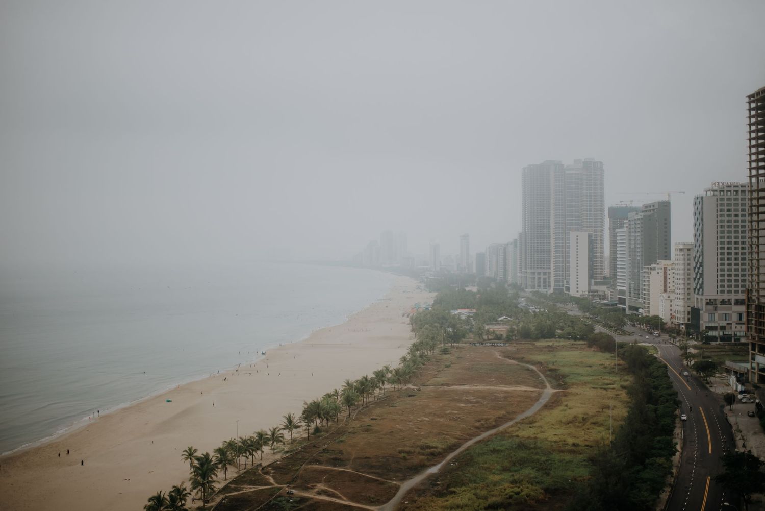 Foggy cityscape of beach and high-rise buildings along coastline on overcast day.
