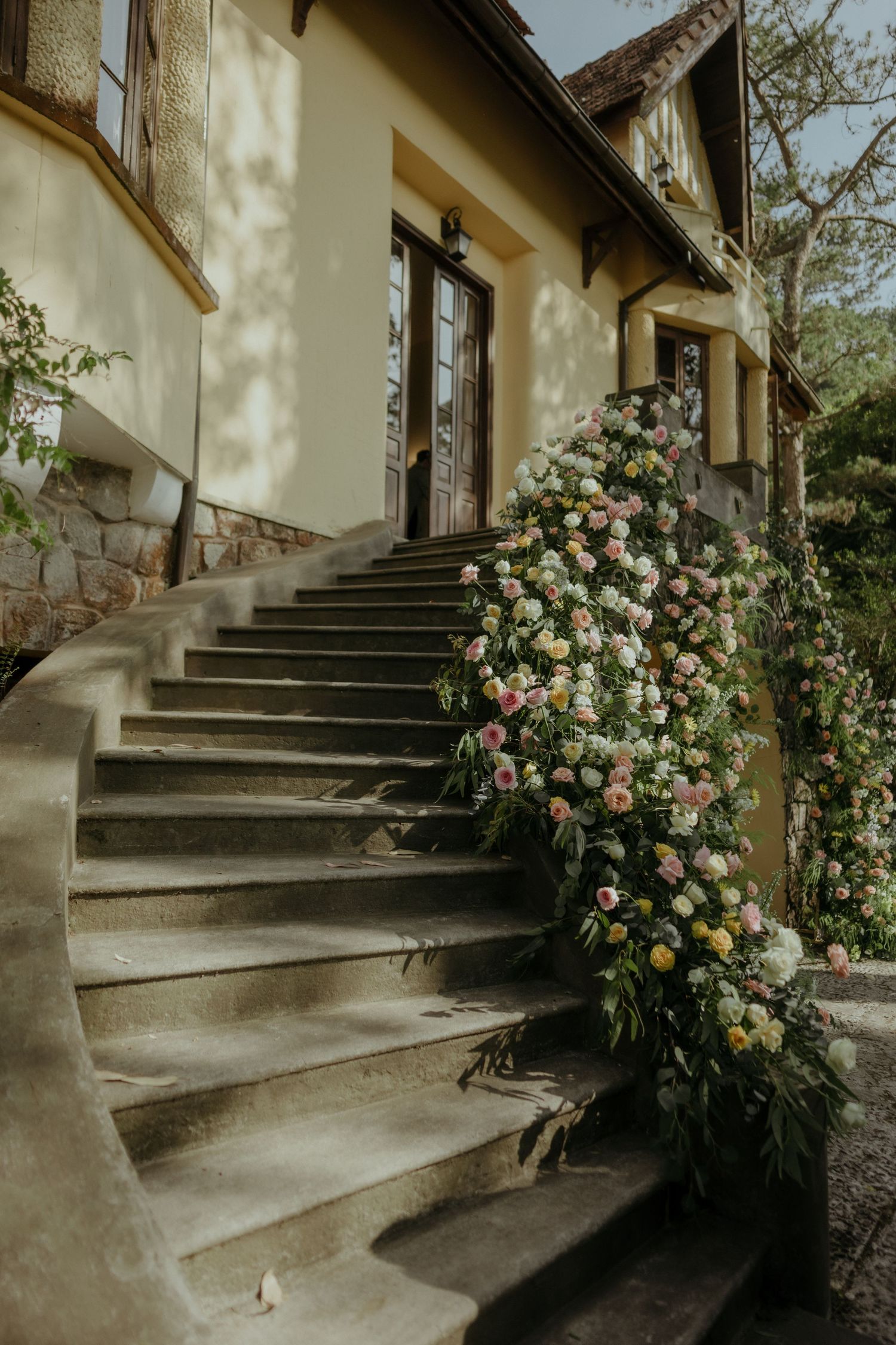 Stone steps leading to an elegant house entrance with climbing roses along the railing in warm vintage tones.