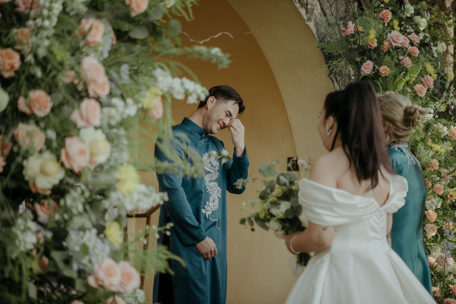 A couple shares a joyful moment under a floral archway decorated with blush pink roses.