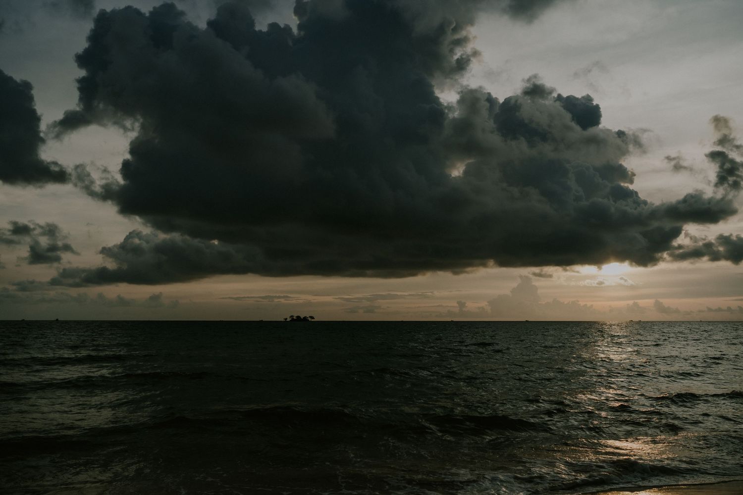 Dramatic seascape with dark storm clouds during sunset over ocean horizon.