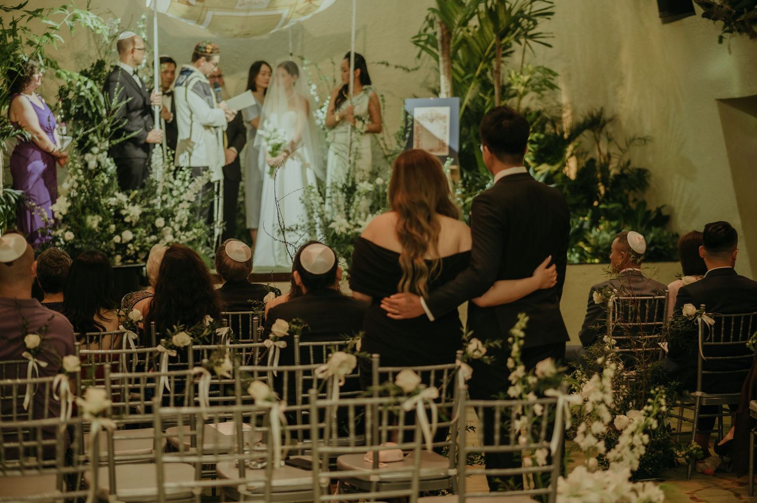 Wedding guests seated in white chairs watching the ceremony from the audience area.