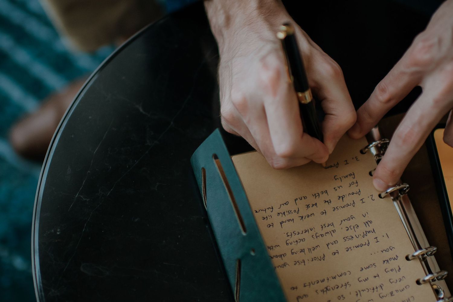 Close-up of hands writing personal message in journal or planner.