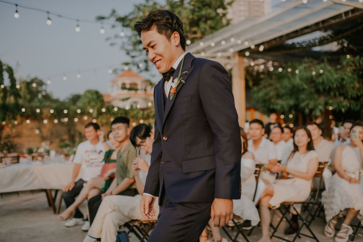 An outdoor wedding ceremony with string lights and guests seated on chairs.