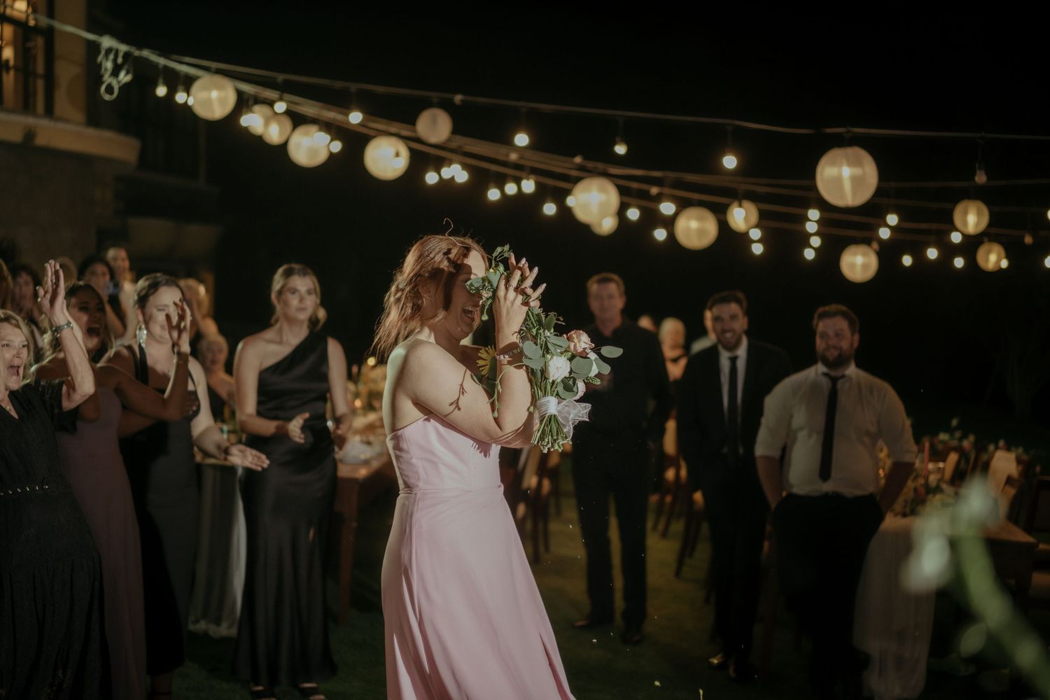 Newlyweds share their first dance under romantic string lights and paper lanterns at an outdoor evening reception.