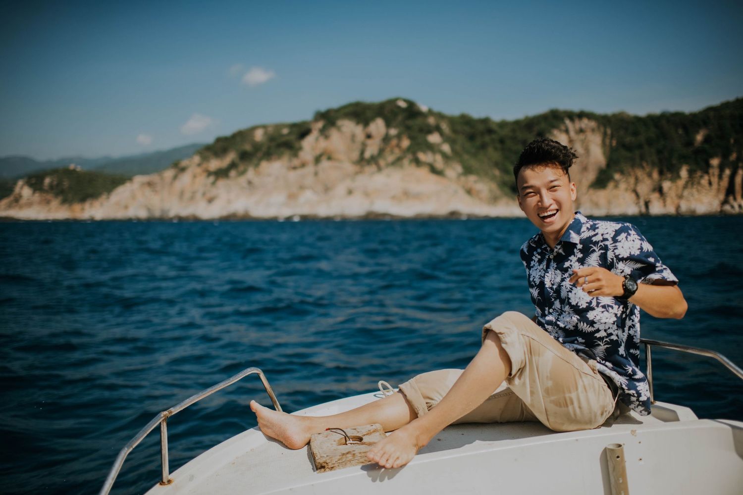 A person relaxes on the bow of a boat with coastal cliffs in the background.