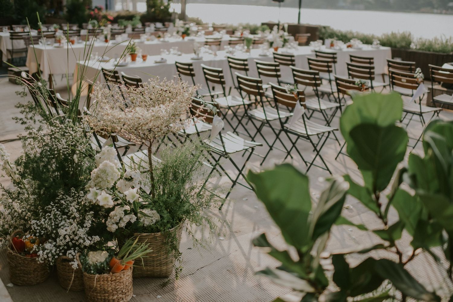Outdoor event space with rustic metal chairs and potted plants on a waterfront patio.