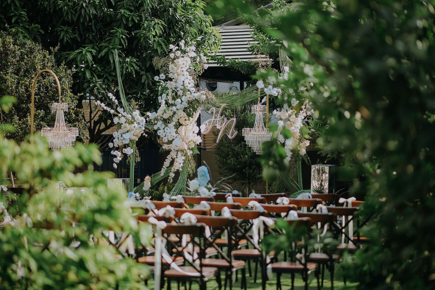 Outdoor wedding reception setup with rustic wooden chairs and floral decorations in garden setting.
