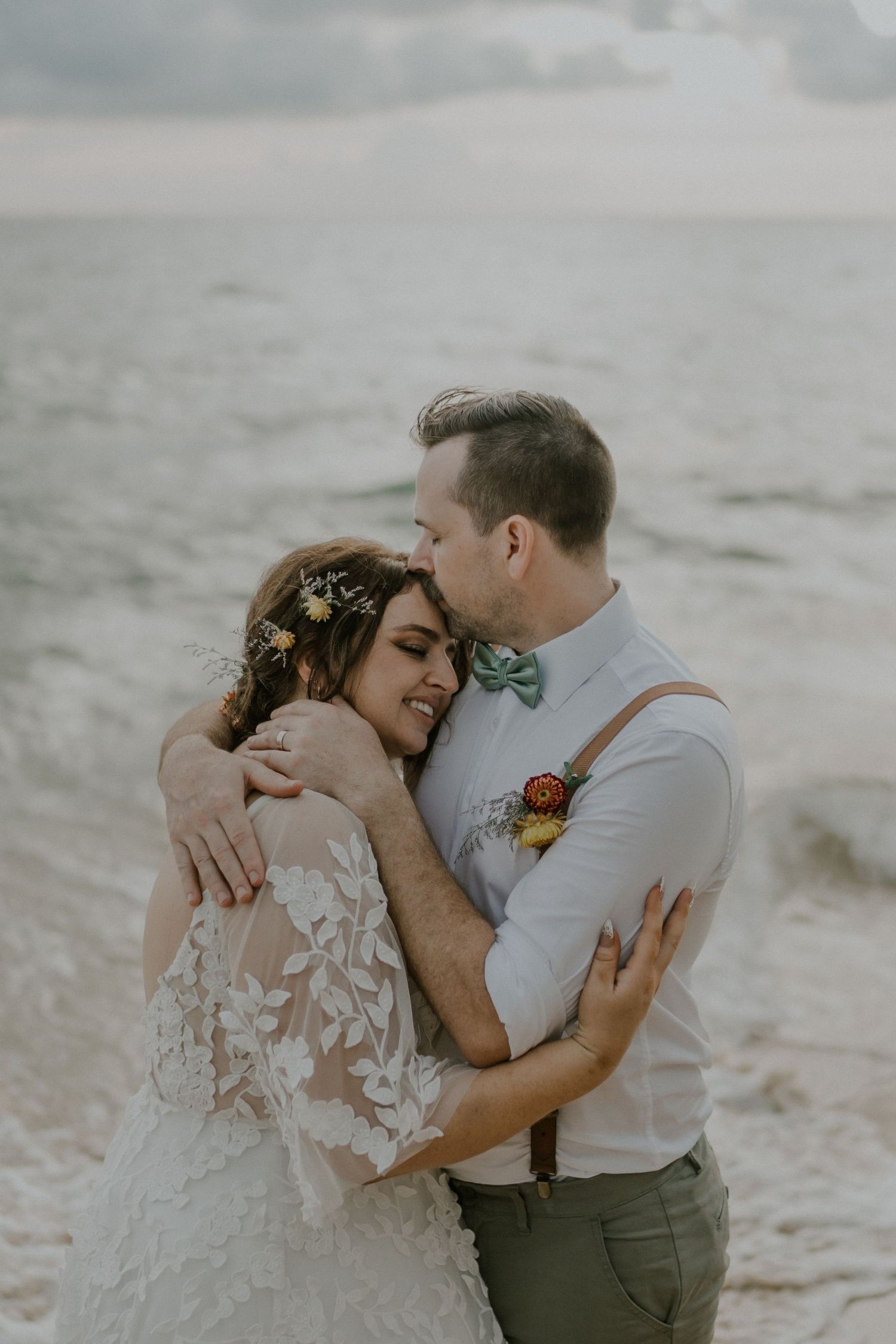Romantic beach wedding portrait capturing intimate embrace with ocean waves in background.