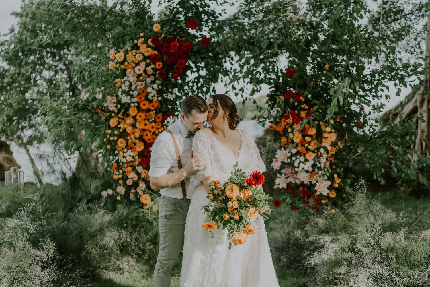 Couple sharing intimate moment under orange and red floral arch in garden setting.