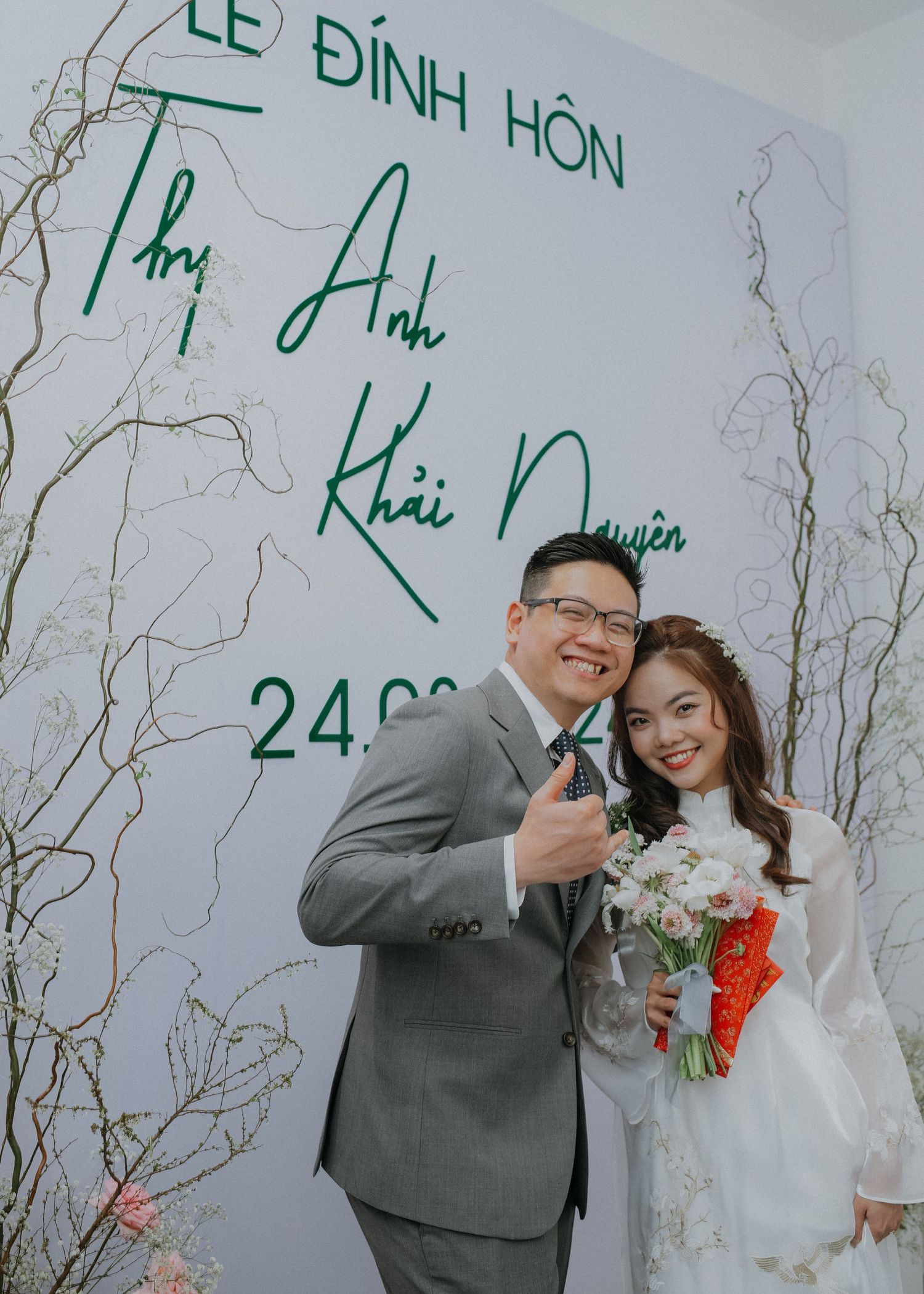A wedding celebration with Vietnamese text backdrop and couple in grey suit and white ao dai.