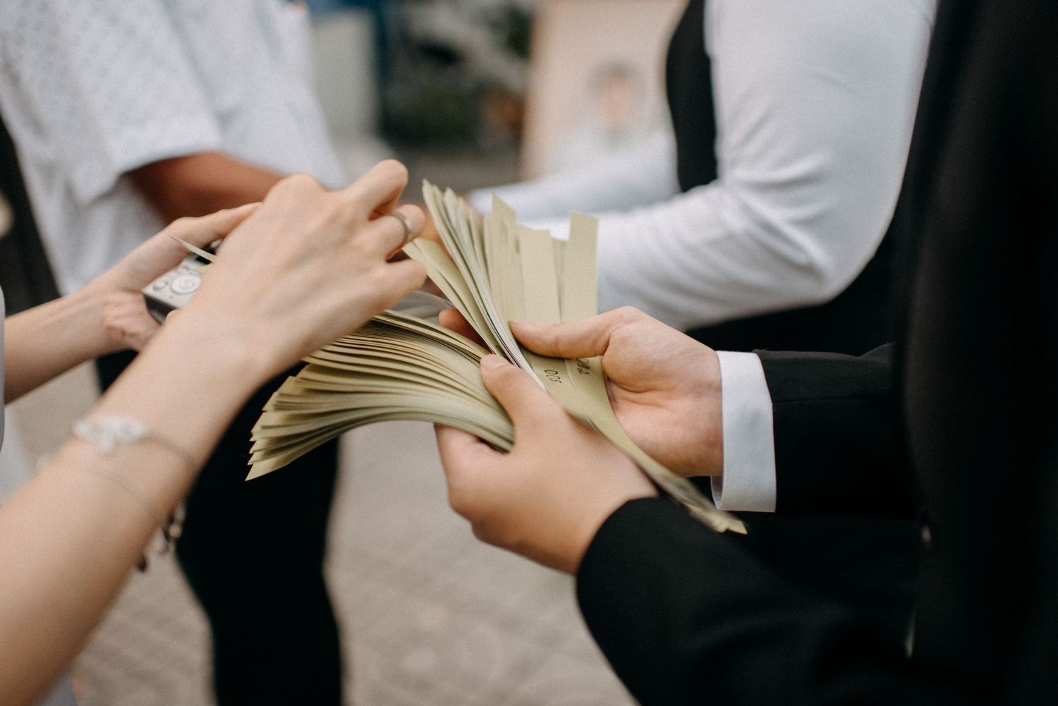 Close-up shot of hands exchanging cash money between two people in formal attire.