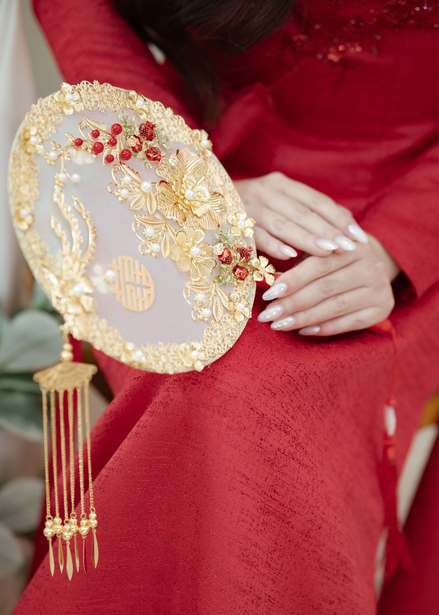 Ornate golden Chinese traditional hand fan with floral details and tassels against a red silk fabric background.