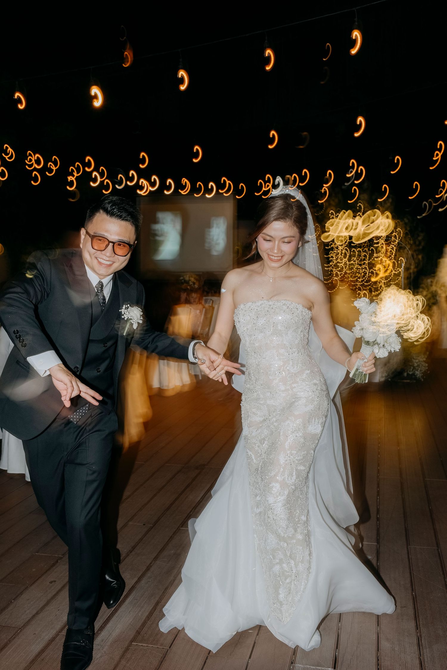 Festive dance moment under decorative string lights on wooden deck at evening reception.