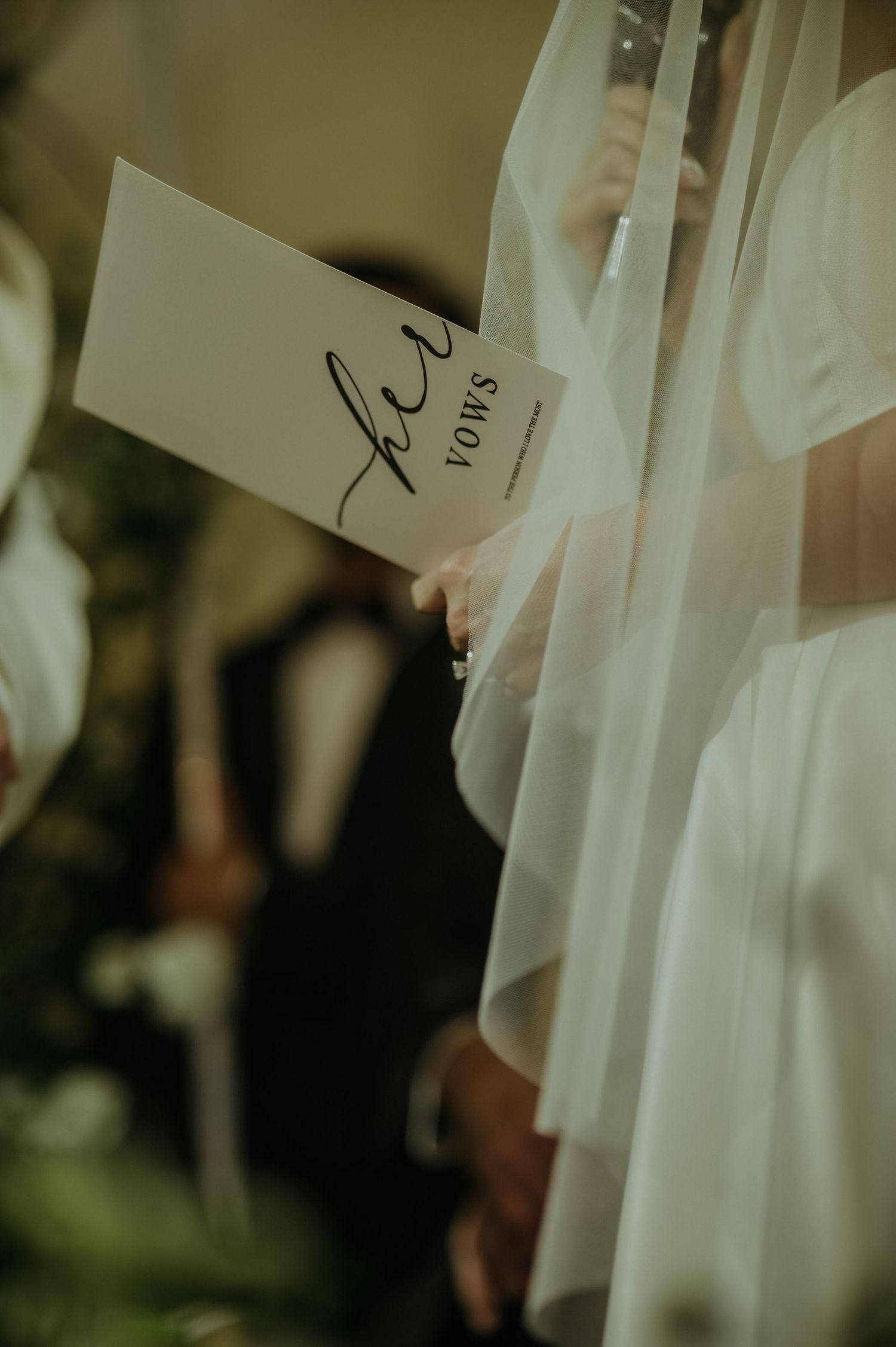 A close-up of wedding vows being held during the ceremony with delicate white veil in the background.