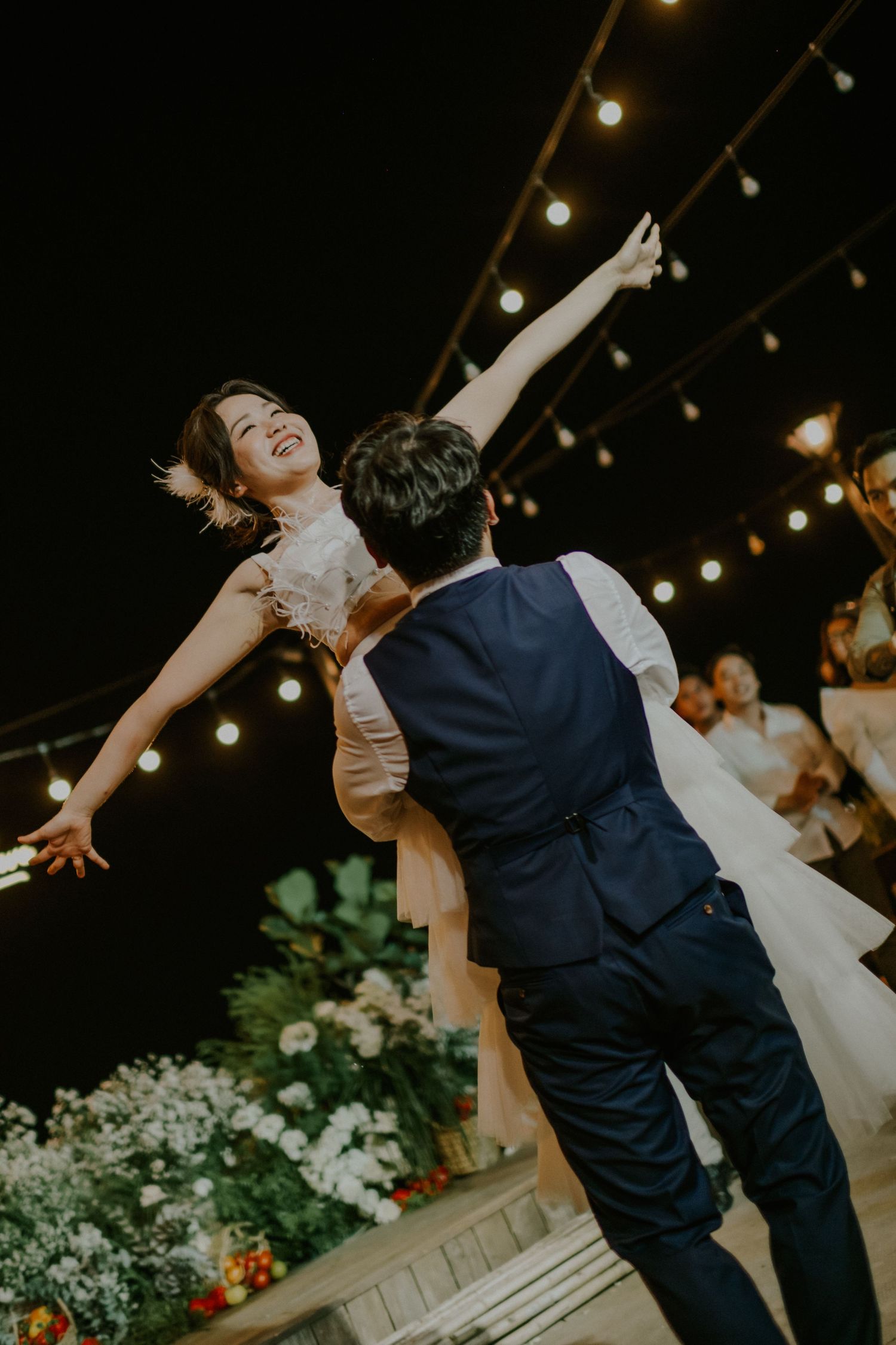 Couple shares romantic dance moment under string lights at outdoor evening wedding reception.