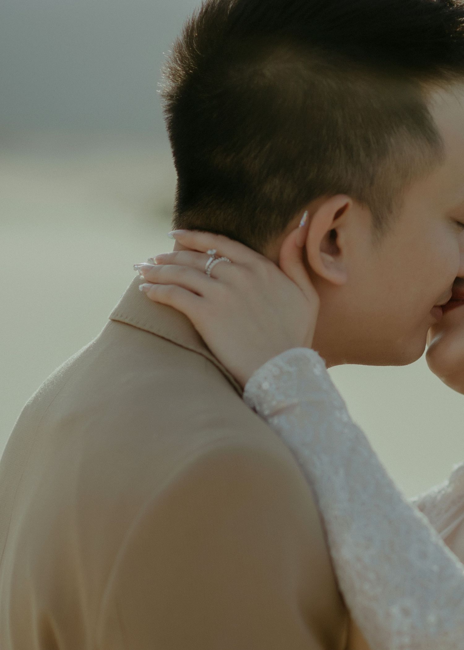 Woman's hand with engagement ring gently caresses partner's neck in intimate moment during romantic photoshoot.