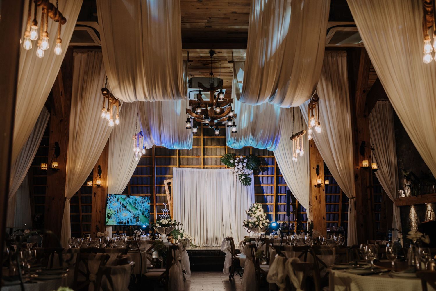 Elegant wedding venue interior with flowing fabric drapes, chandeliers and romantic lighting.