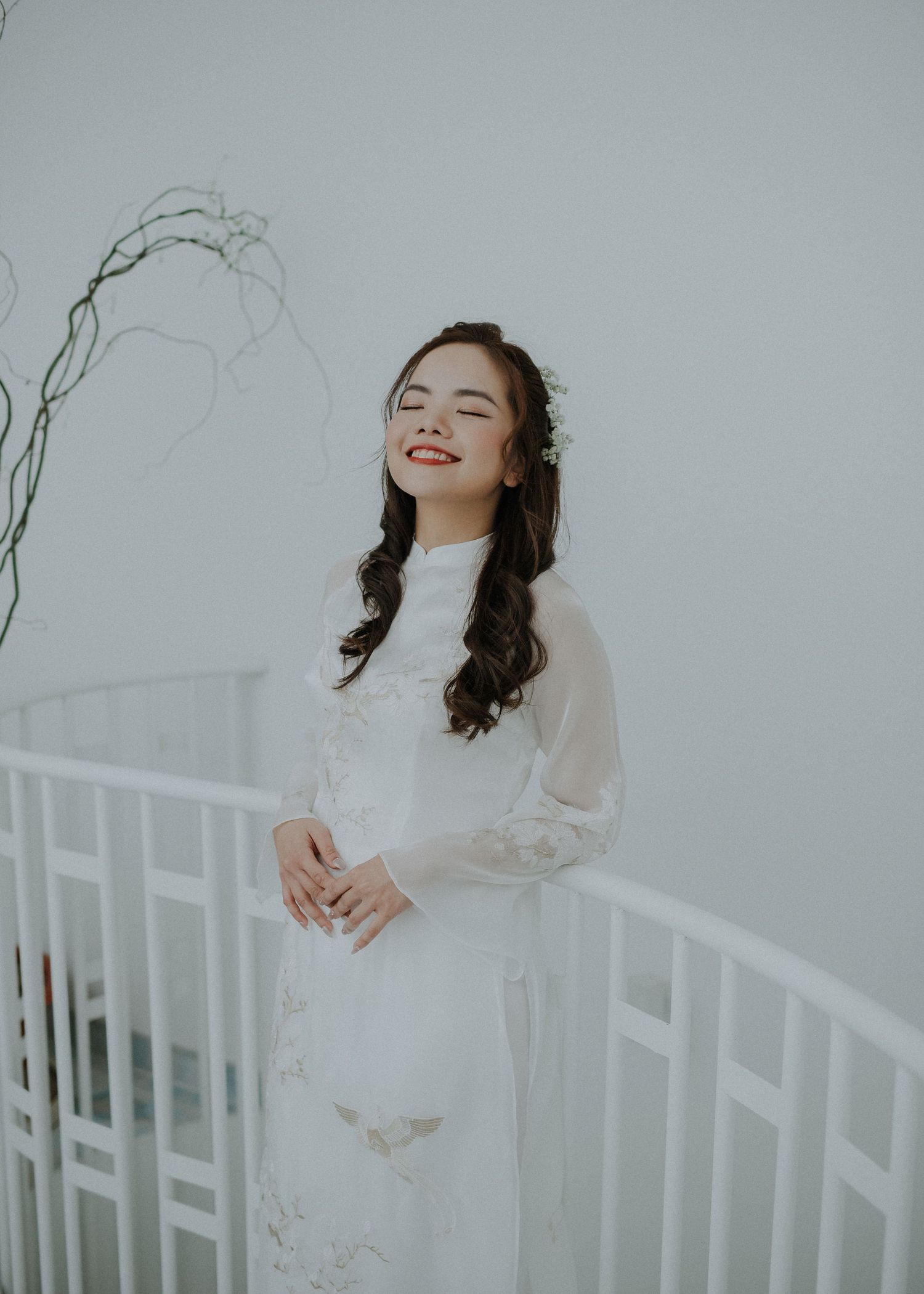 Bride in traditional white ao dai dress poses against minimalist background with natural smile.