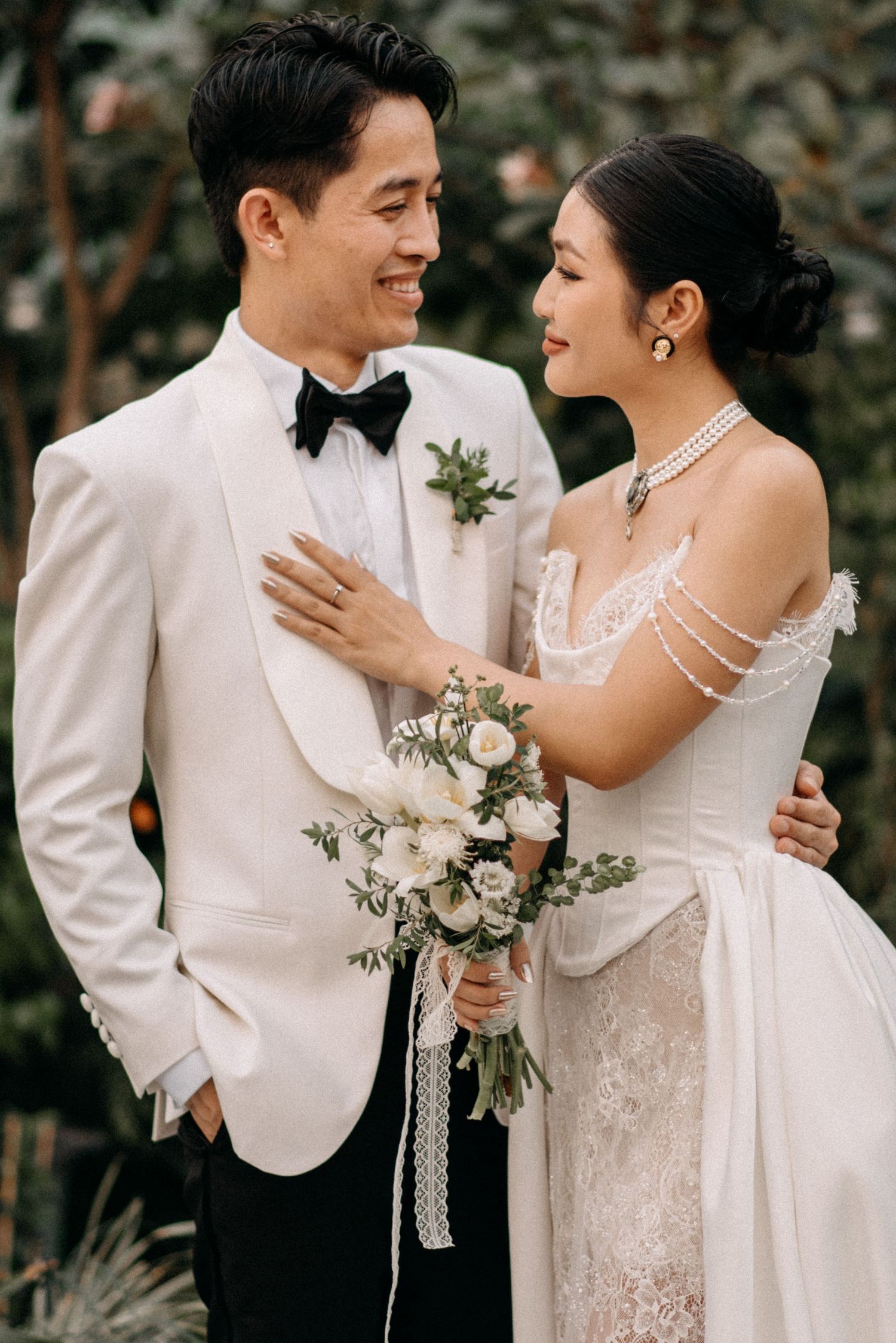 Romantic wedding portrait of a couple in white attire smiling at each other outdoors.