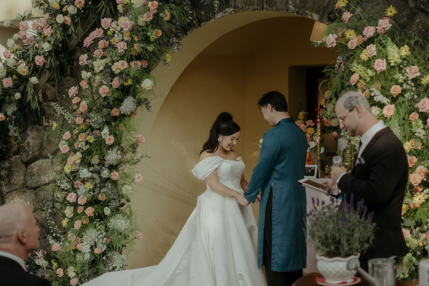 A romantic wedding ceremony takes place under an archway adorned with blush pink roses.