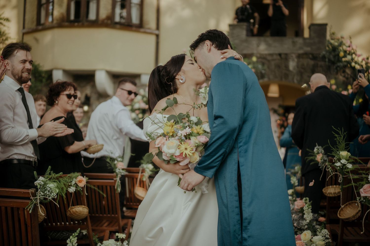Couple shares intimate moment during wedding ceremony in church surrounded by floral arrangements and guests.