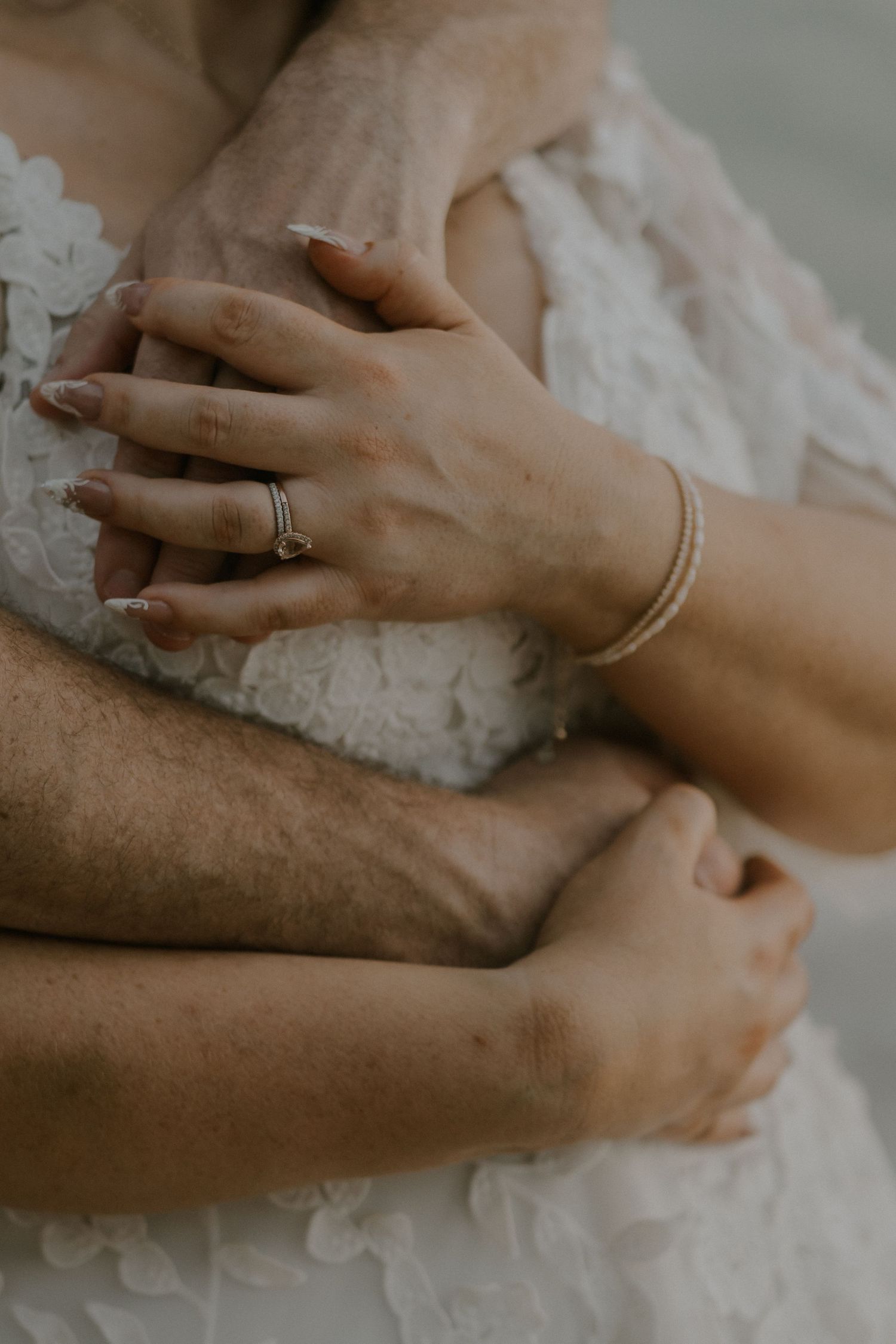 Close-up of wedding rings and delicate lace details with hands embracing.