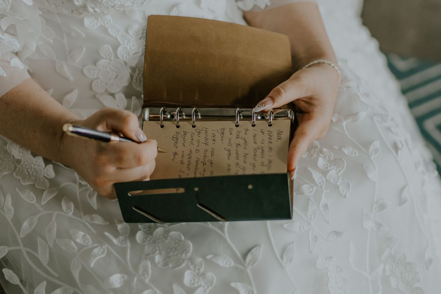 Hands writing in a small notebook while wearing a white lace dress.
