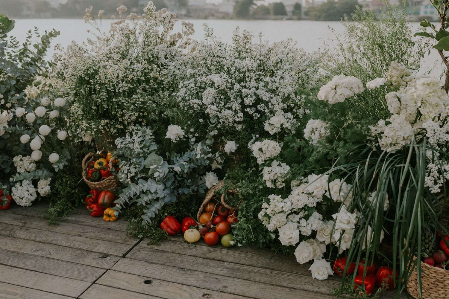 White floral arrangements with orange and red accents line a wooden deck railing at an outdoor venue.