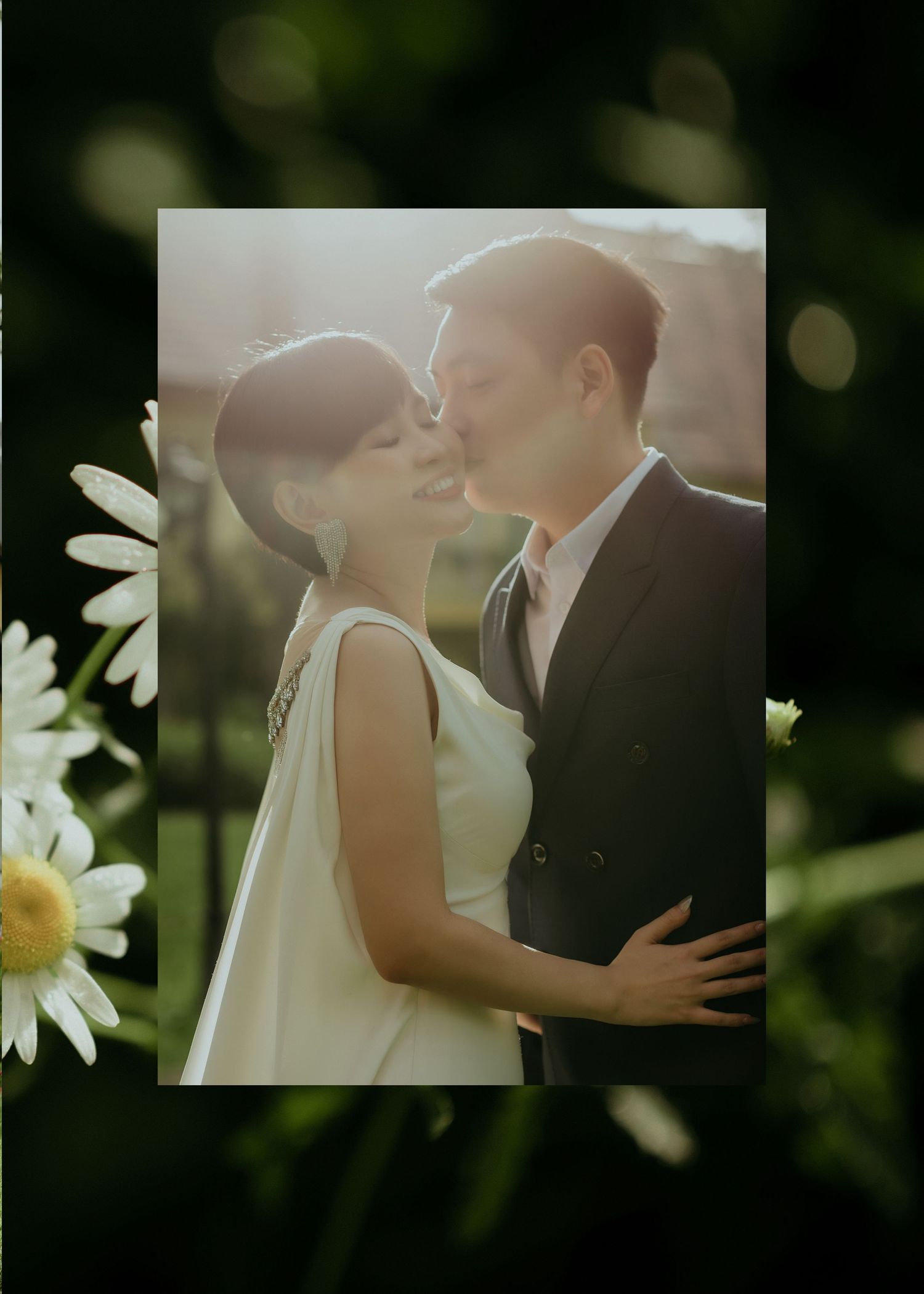 A romantic wedding portrait surrounded by daisies shows a couple sharing an intimate moment in soft sunlight.