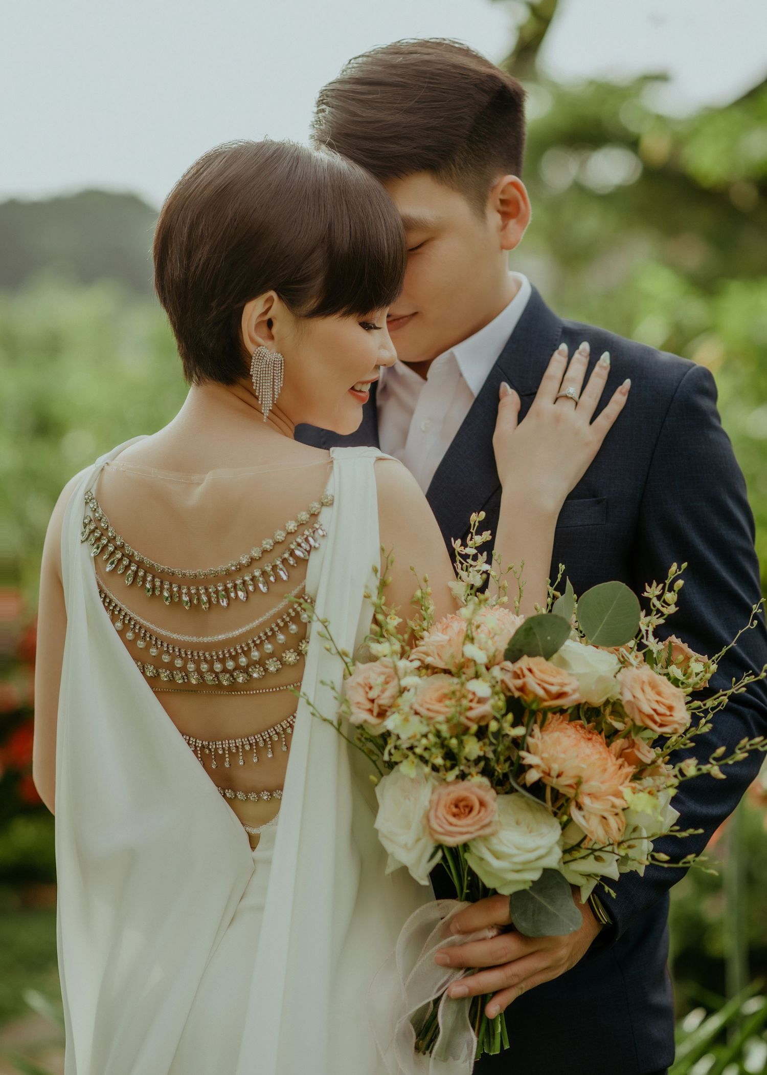 A romantic wedding photo showcases a bride in an elegant white dress with jeweled back detail and a peach floral bouquet.
