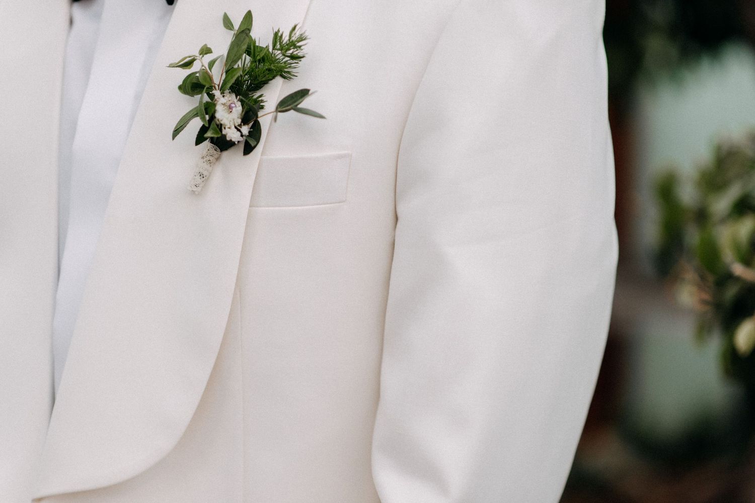 Detail shot of white tuxedo jacket with boutonniere flower decoration.