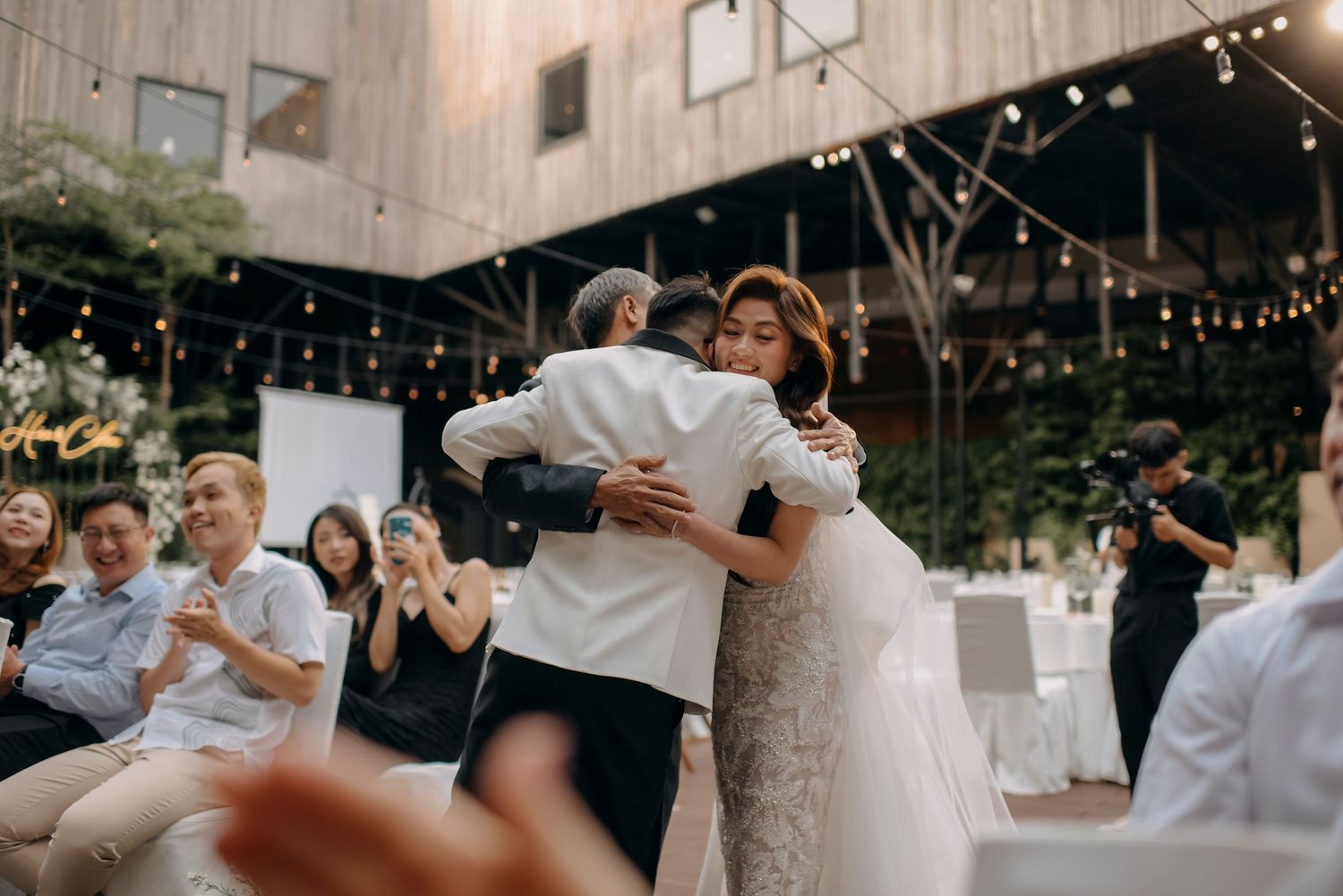 Intimate moment during wedding reception dance under string lights at rustic venue.